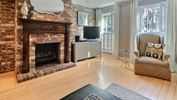 A living room with a brick fireplace, a television, a sofa, and a window with curtains. - Heated Pool Access | 5*Clean | Flex Cancelation (Savannah)