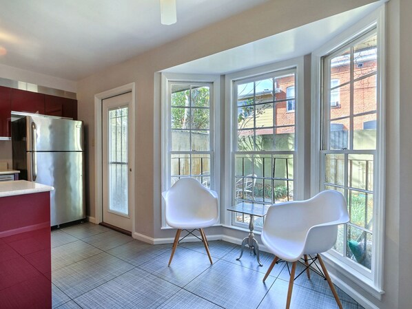 A modern kitchen with a stainless steel refrigerator, a dining area with two white chairs, and large windows offering a view of the outside. - Heated Pool Access | 5*Clean | Flex Cancelation (Savannah)