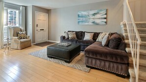 A living room with a brown sofa, a black ottoman, and a patterned rug. - Heated Pool Access | 5*Clean | Flex Cancelation (Savannah)