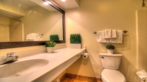 Un baño con lavamanos, espejo, inodoro y dos plantas en macetas.