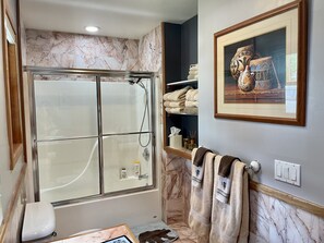 A bathroom with a glass-enclosed shower, marble walls, a toilet, and a shelf with towels and toiletries. - Oh Be Joyful!! House - One block from Camp4 Coffee (Crested Butte)