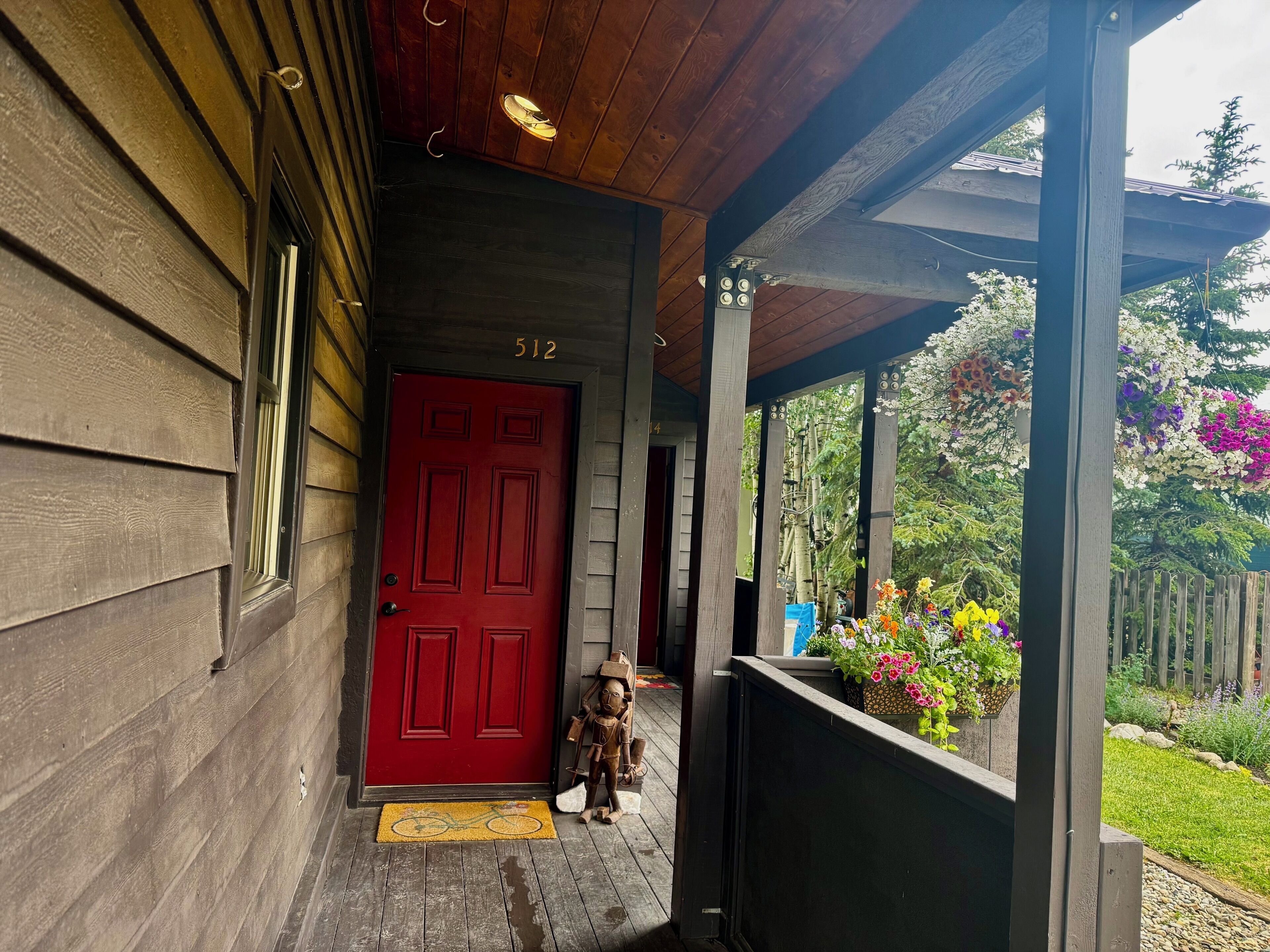 Une maison en bois avec une porte rouge, portant le numéro 512, et un porche avec un paillasson.