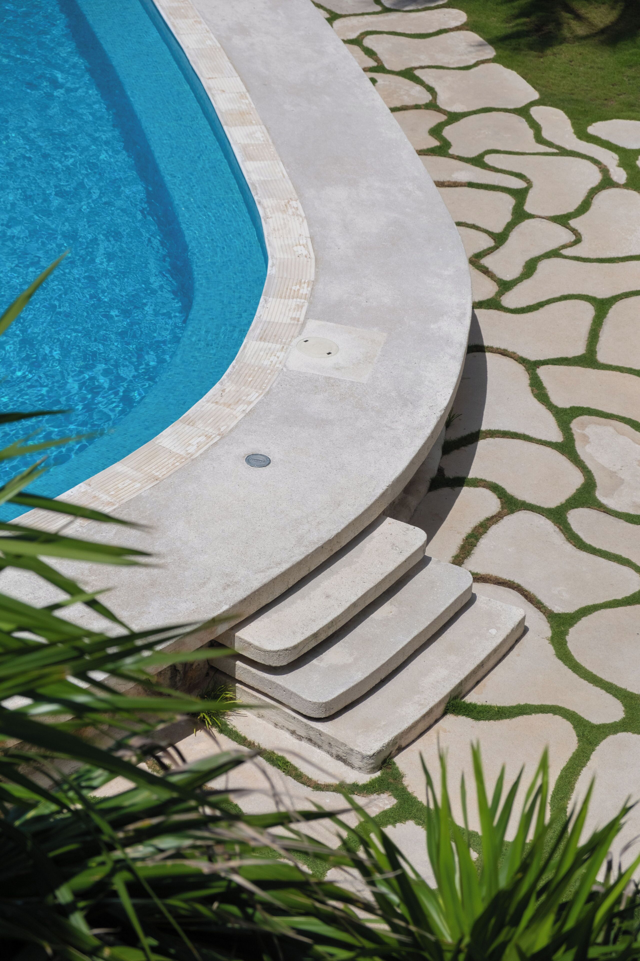 Una piscina con borde de piedra y escalones de acceso, rodeada por un camino de piedra con diseño.