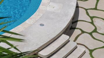 Una piscina con borde de piedra y escalones de acceso, rodeada por un camino de piedra con diseño.