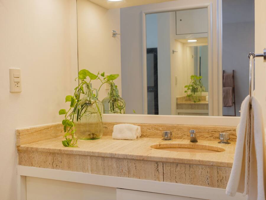 Un baño con encimera color beige, un lavabo, un espejo y un perchero para toallas.