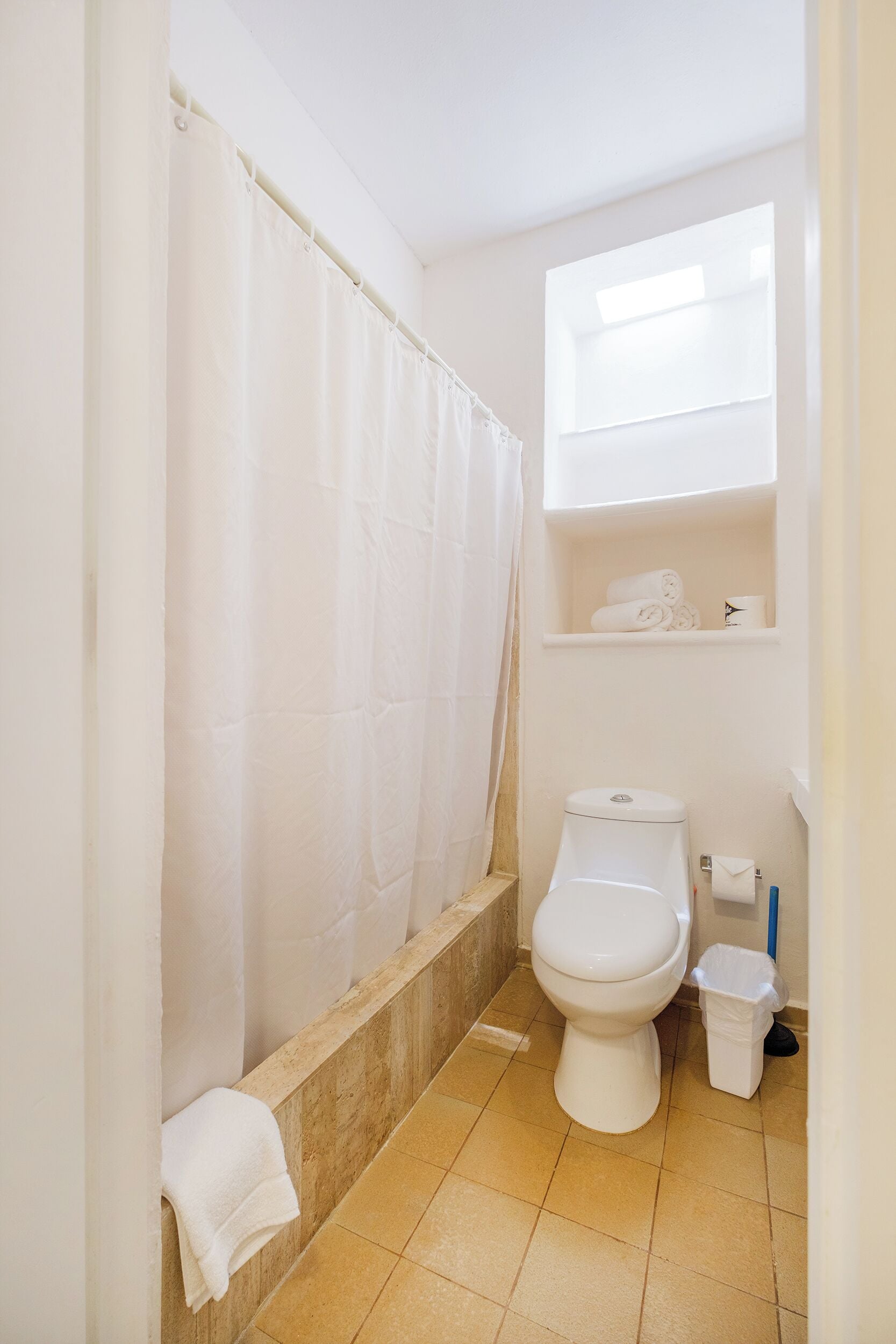 Et badeværelse med badekar, toilet og en hylde med håndklæder.