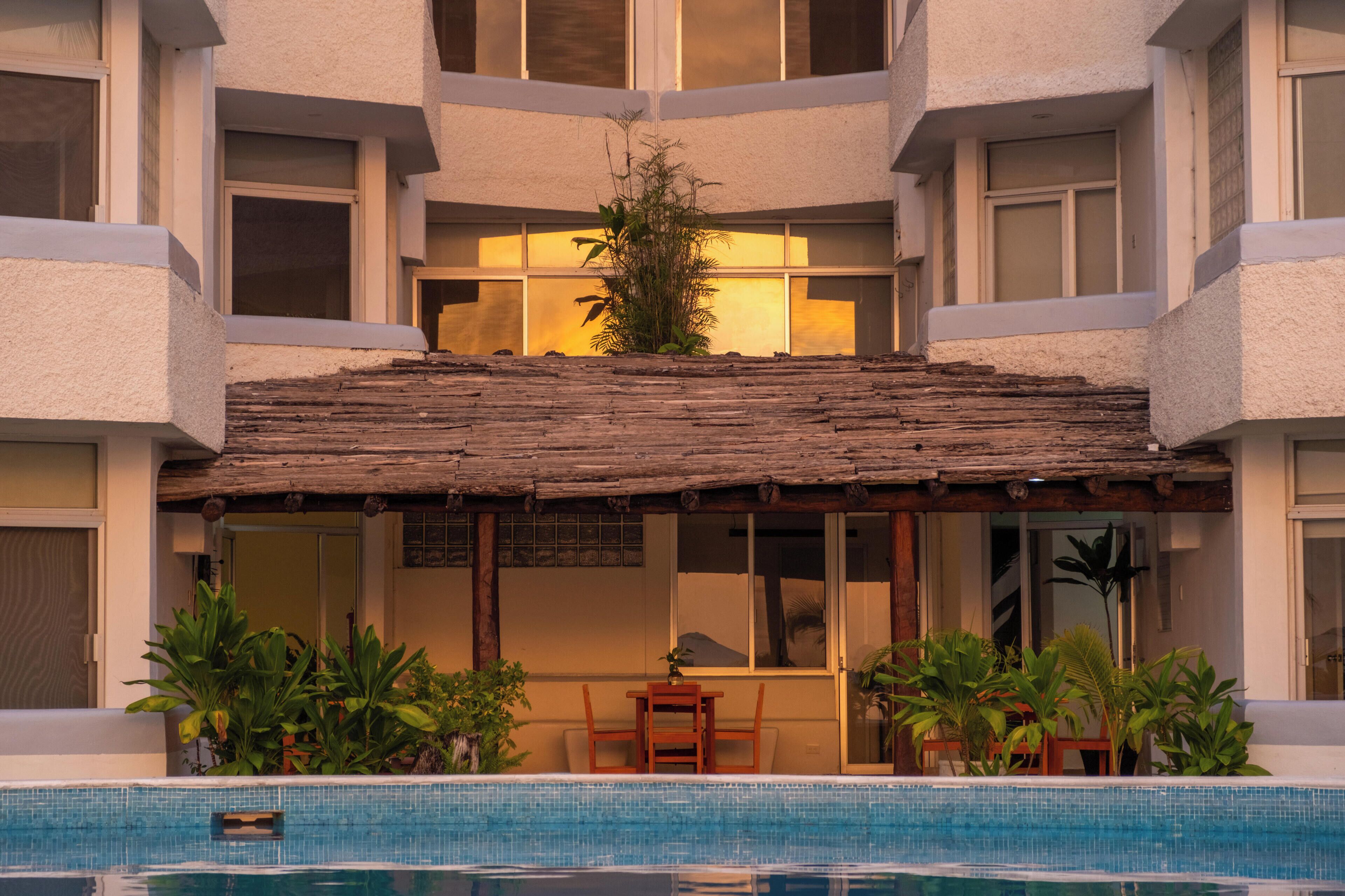 A hotel with a pool, a covered outdoor seating area, and a building facade with large windows.