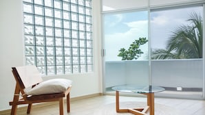 Una habitación con una silla de madera, una mesa de vidrio y vistas a un balcón con palmeras.