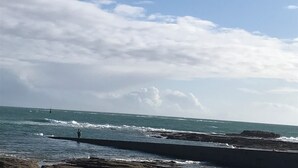 Vista costera con costa rocosa, olas y cielo despejado.