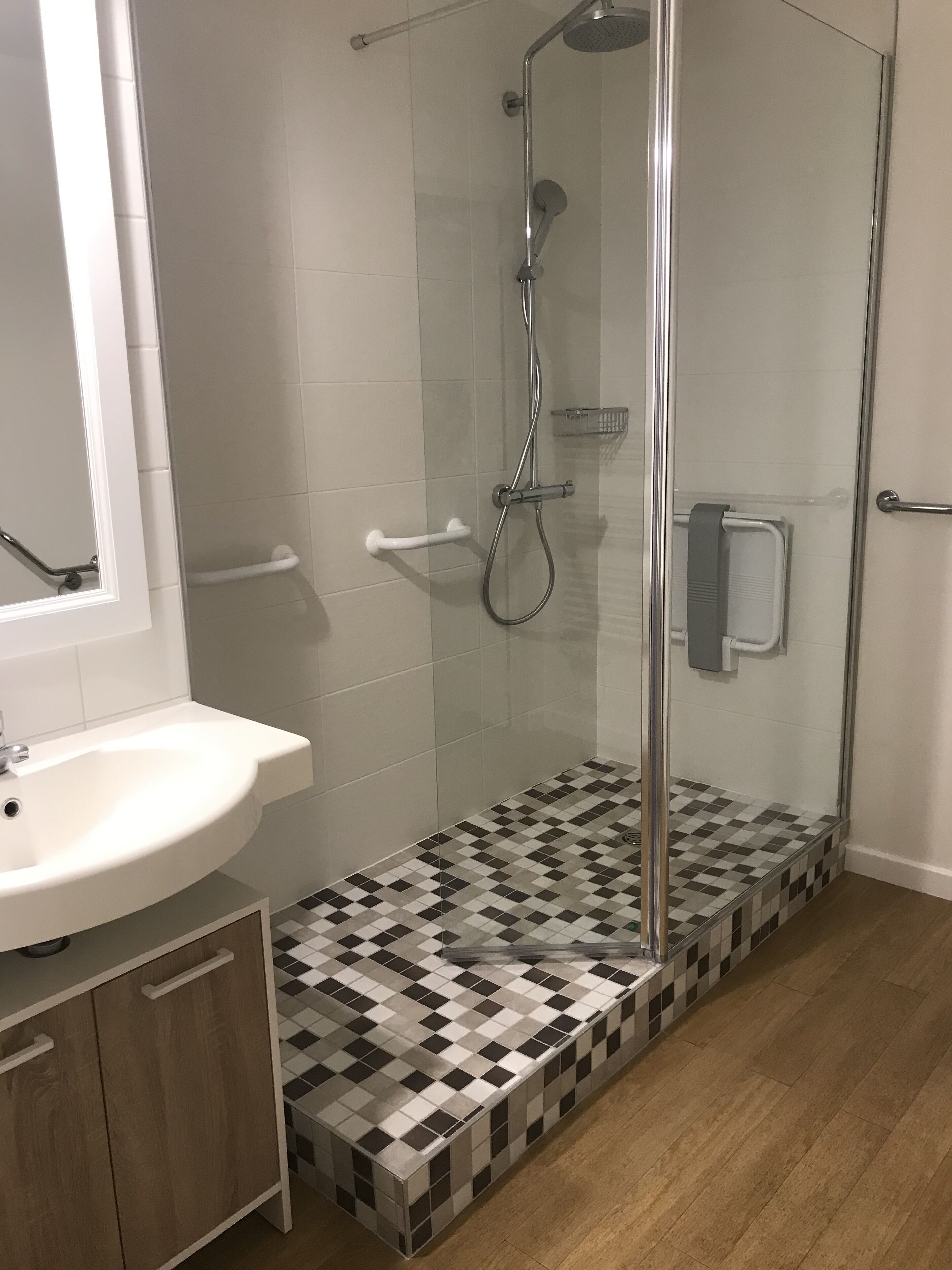Une salle de bain avec une douche à parois de verre, un lavabo blanc et un carrelage à motifs géométriques.
