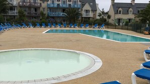 Un área de piscina con sillas de descanso azules y una piscina con borde de azulejos.