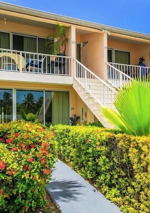 Un edificio de dos plantas con un balcón, una escalera y un jardín bien cuidado con diversas plantas.