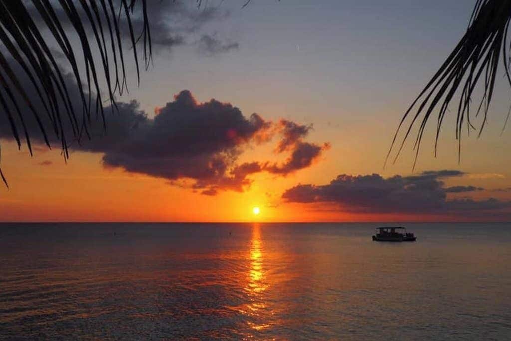 Solnedgang over et roligt hav med en båd i det fjerne.