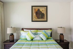 Ein Hotelzimmer mit einem Bett, zwei Nachttischlampen, einem gerahmten Kunstwerk an der Wand und einem Fenster mit Vorhängen.