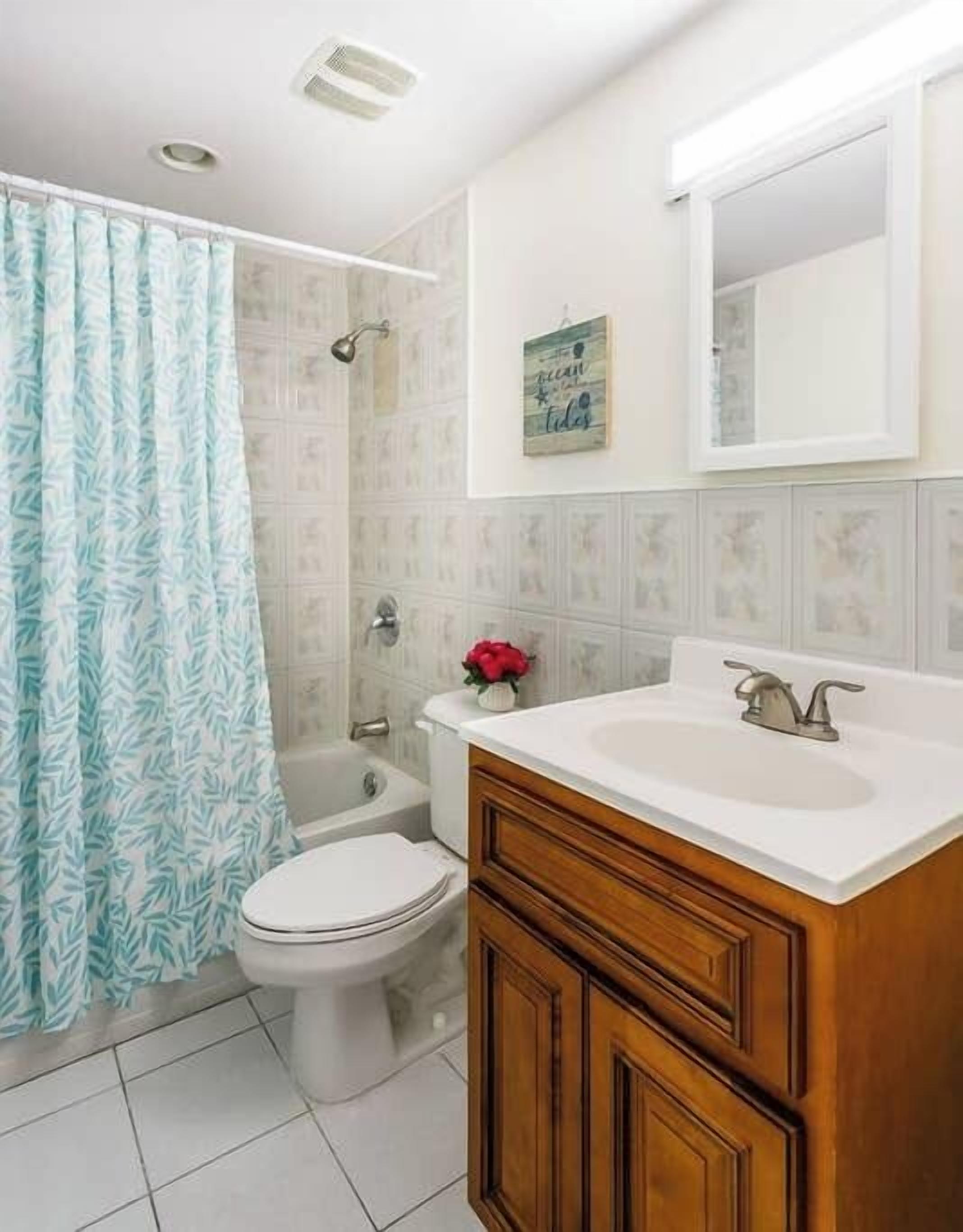 Un baño con cortina de ducha, inodoro, lavamanos y espejo.