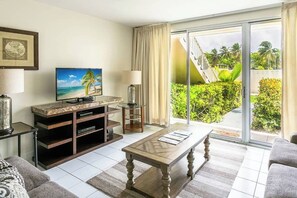 Ein Hotelzimmer mit Fernseher, einem Holztisch, einer Couch, einer Glastür, die auf einen Balkon mit Blick auf Grünflächen führt, und einer Treppe.