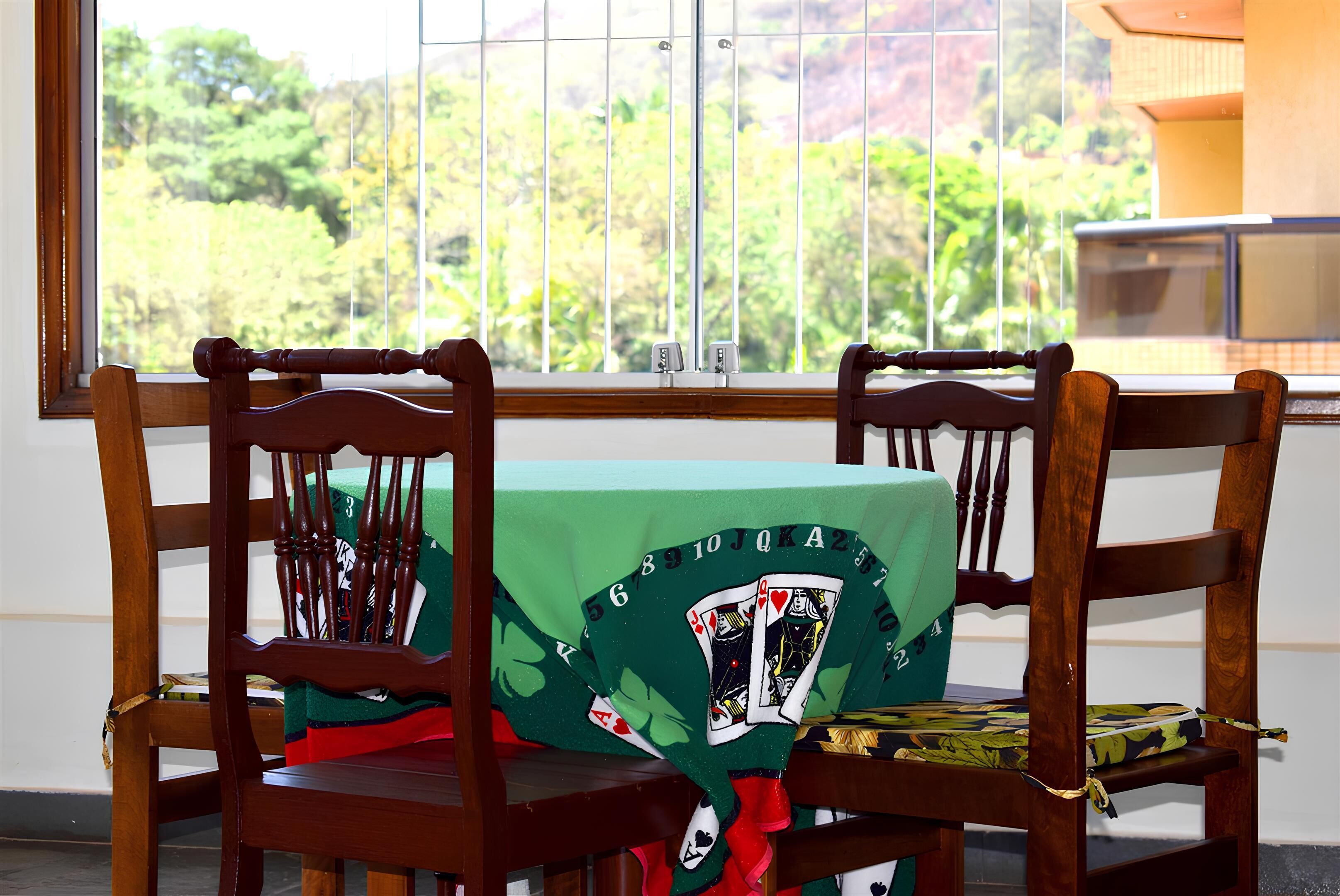 A room with a view of trees through a window, a wooden chair, and a table with a green tablecloth.