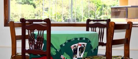 A room with a view of trees through a window, a wooden chair, and a table with a green tablecloth.
