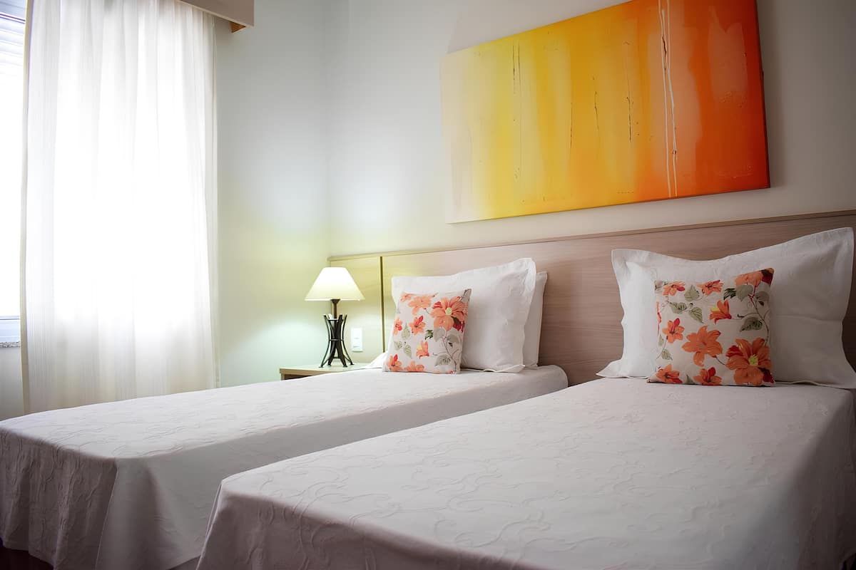 Une chambre d’hôtel avec deux lits, une table de chevet avec une lampe et un grand tableau abstrait accroché au mur.