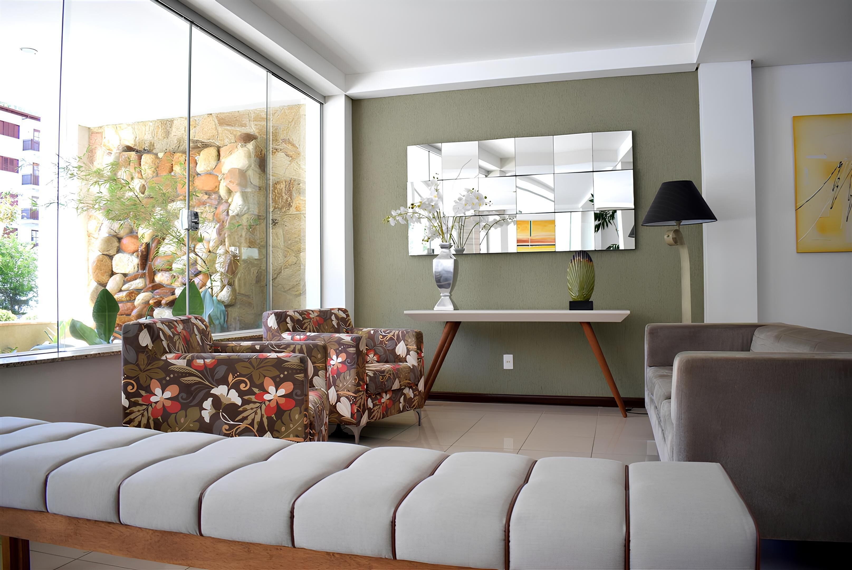 A living room with a sofa, chairs, a coffee table, a lamp, a mirror, and a decorative wall.