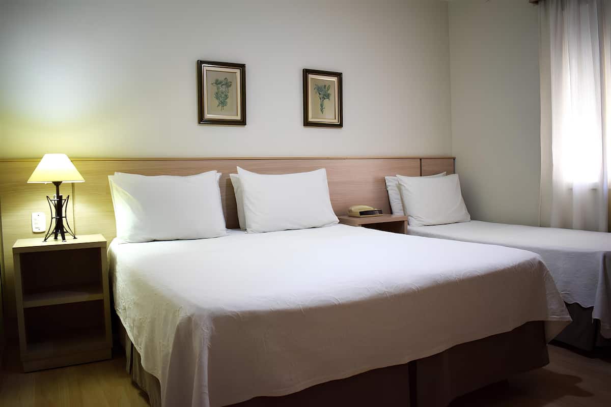 Une chambre d’hôtel avec deux lits, une table de chevet avec une lampe et deux tableaux encadrés au mur.