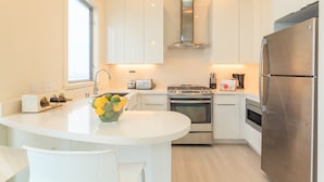 Una cocina moderna con muebles blancos, un refrigerador de acero inoxidable, un horno empotrado y una isla central con un frutero.