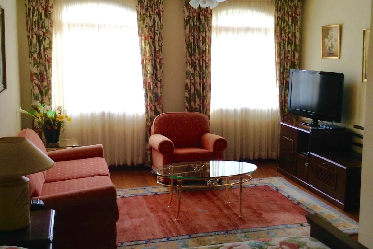 A living room with a red armchair, a glass coffee table, a television, and floral curtains.