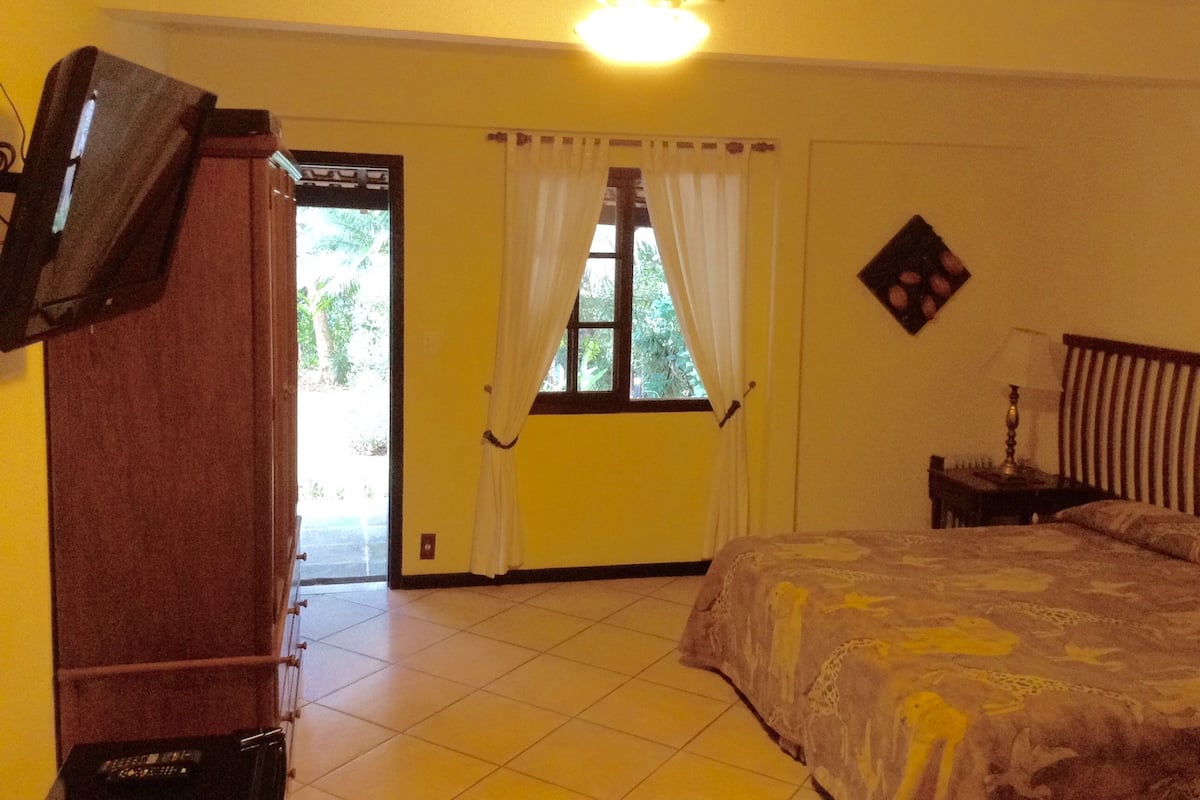 A room with a bed, a ceiling fan, a television mounted on the wall, and a window with curtains.