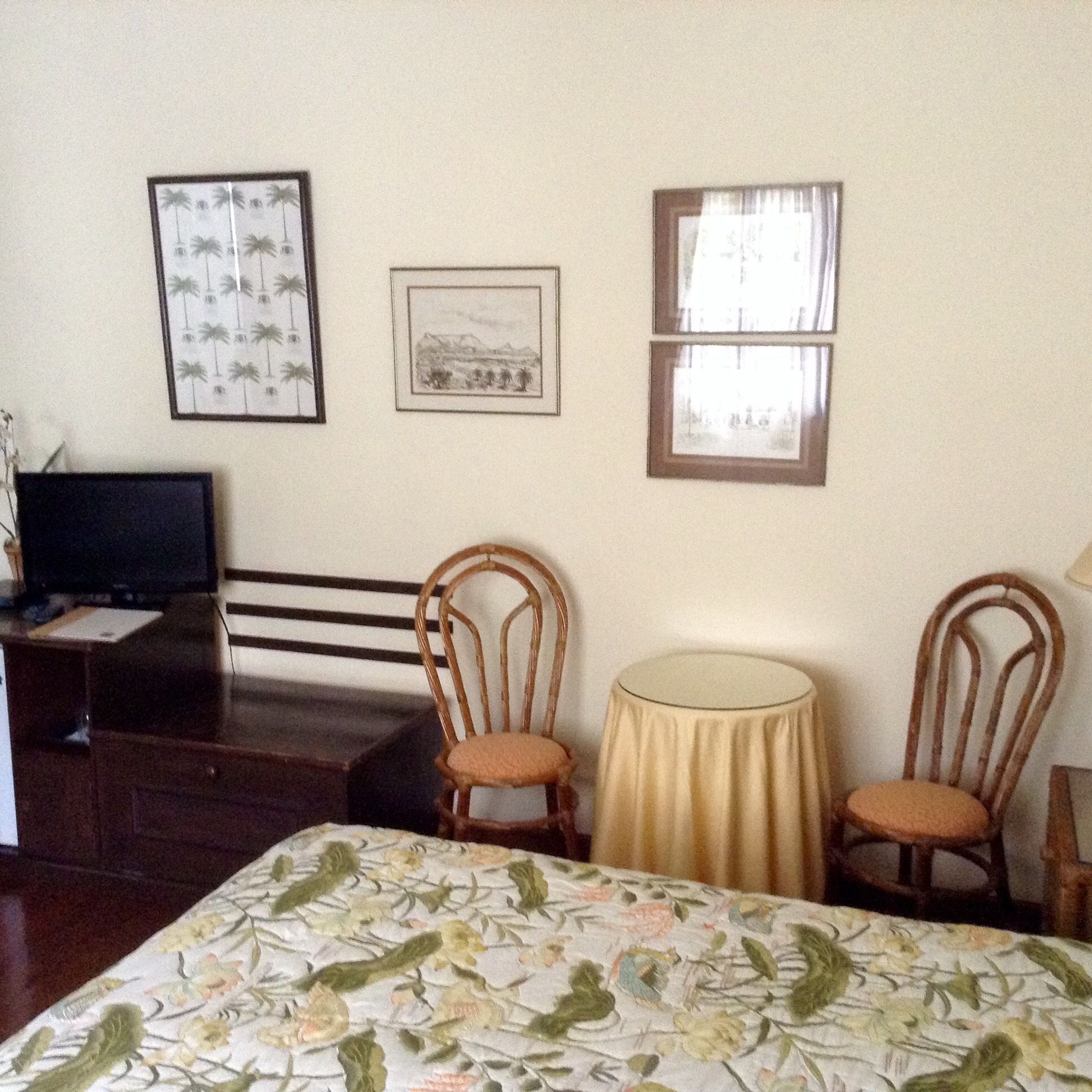 A hotel room with a bed, two wooden chairs, a small round table, a television on a desk, and three framed pictures on the wall.