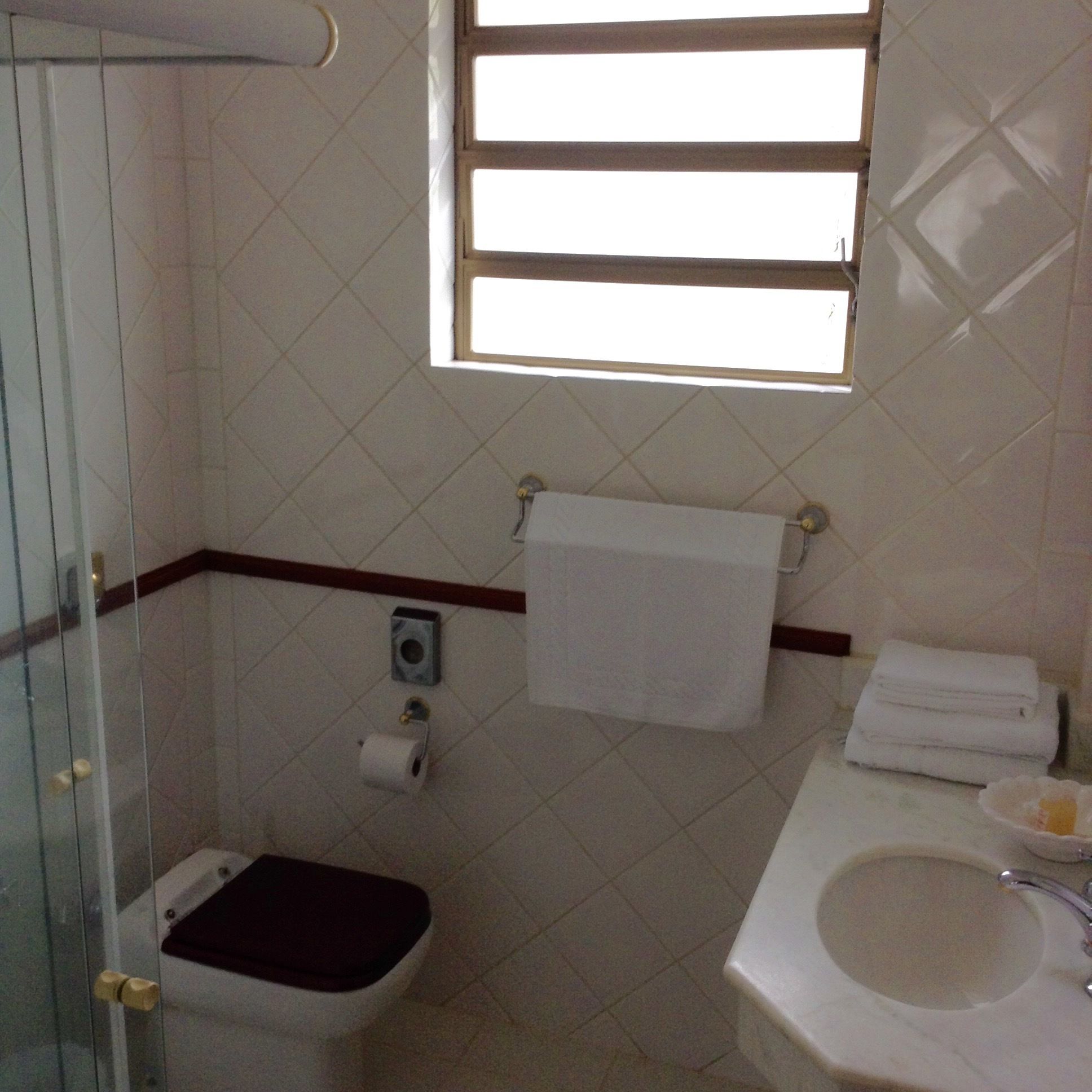Casa de banho com sanita, lavatório, janela e suporte para toalhas.