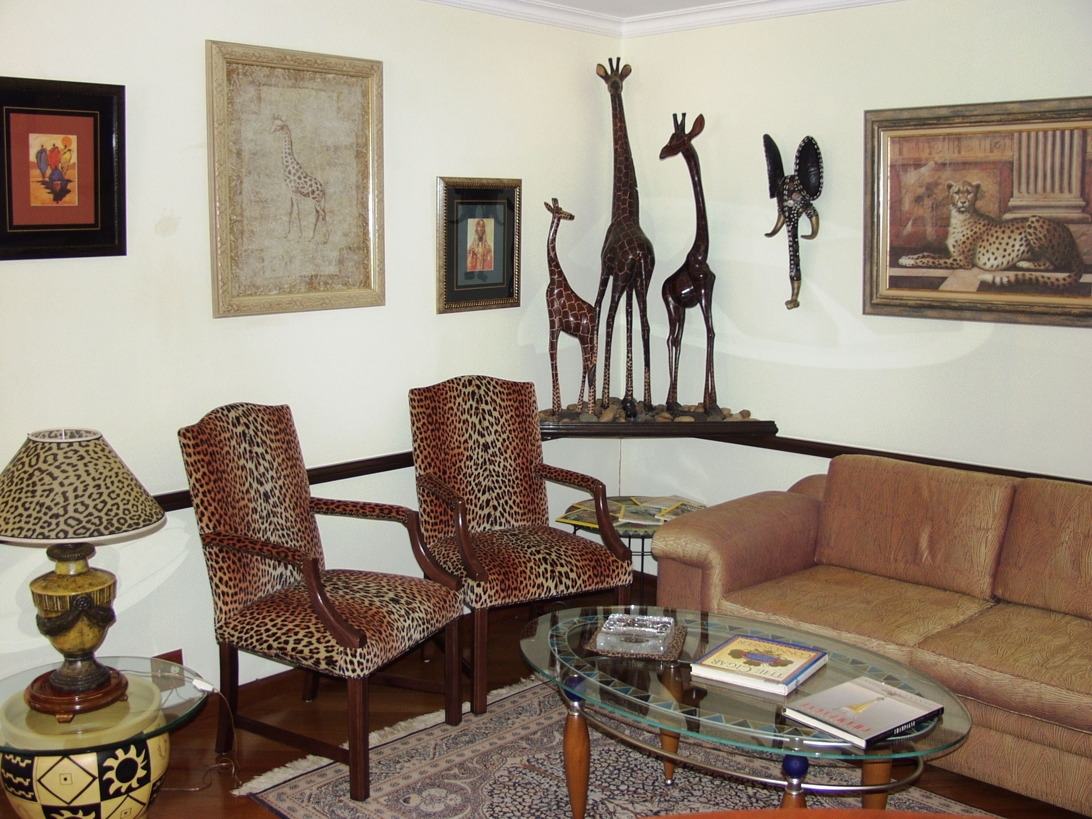 Ein Wohnzimmer mit Leopardenmuster-Sesseln, einem Glastisch, einer Couch und einer Lampe.