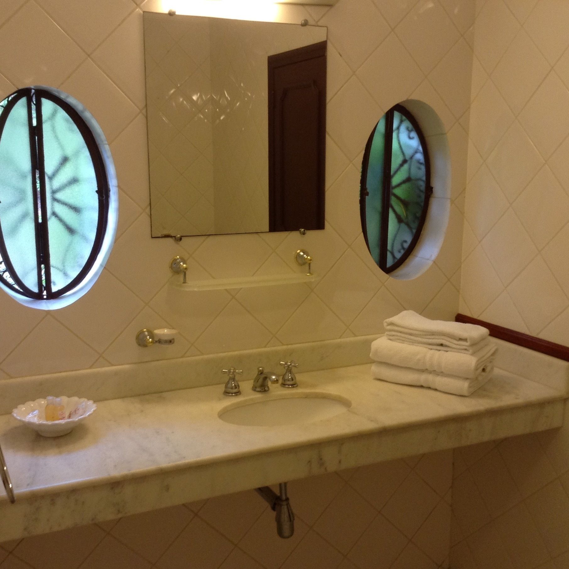 A bathroom with a sink, two round mirrors, a towel stack, and a small dish on the counter.