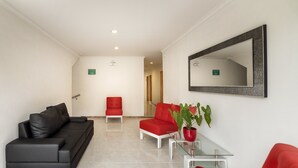 A modern lobby with a black sofa, a red armchair, a glass coffee table, and a potted plant.