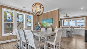 Una cocina moderna con armarios blancos, un comedor con sillas blancas y un amplio ventanal con una pintura de un velero.