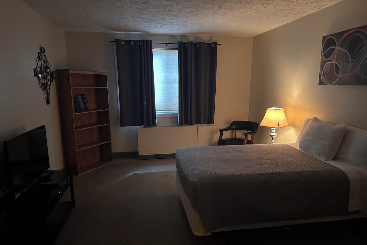 Hotelkamer met een bed, bureau, stoel, televisie, boekenplank en raam met gordijnen.