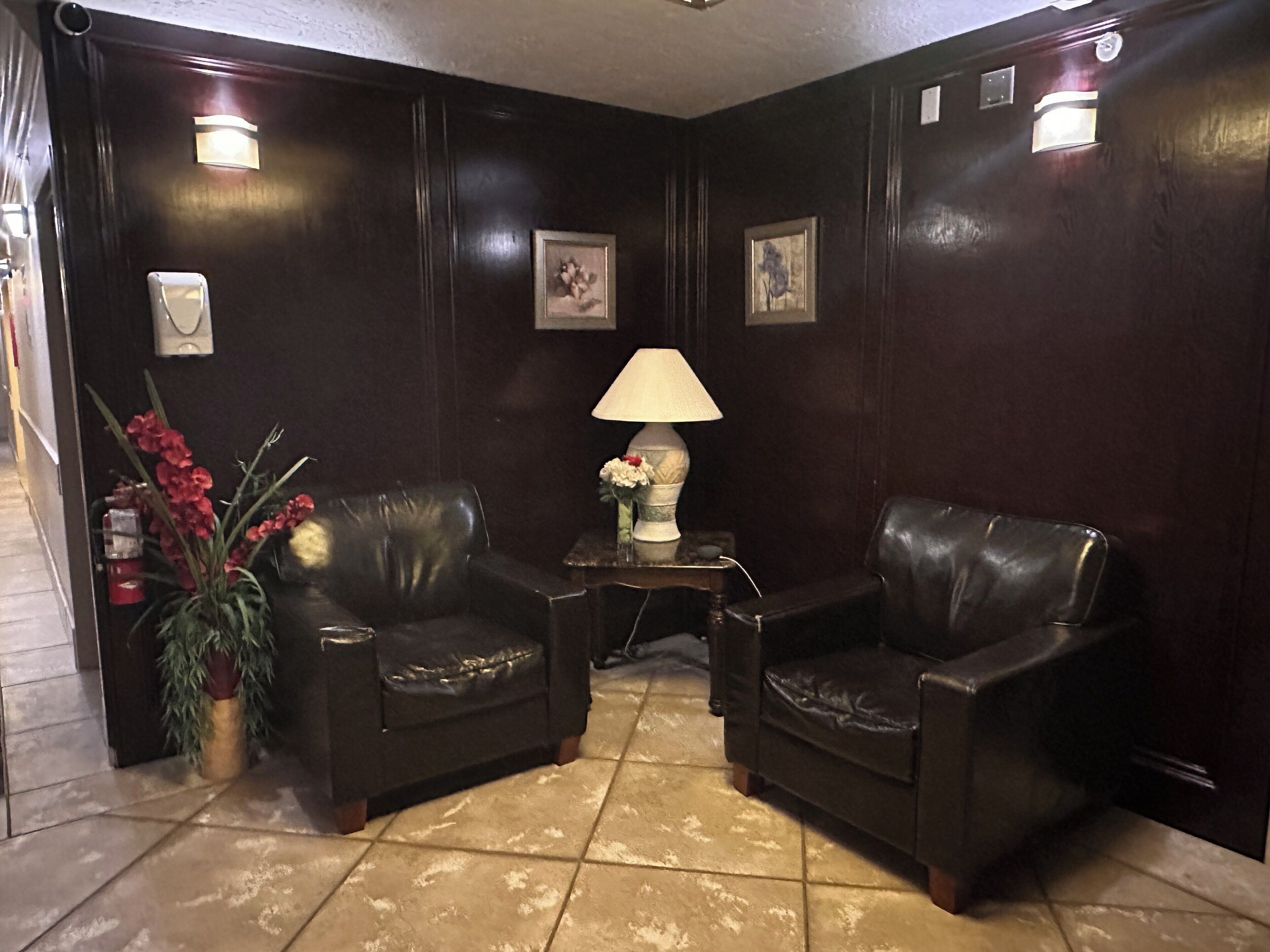 A dark wooden room with two leather chairs, a small table with a lamp, and a vase with flowers.