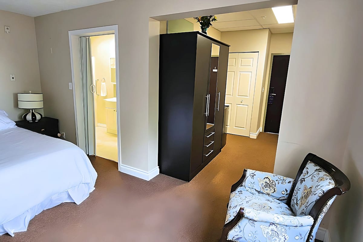 Een hotelkamer met een bed, een stoel, een kledingkast en een badkamer zichtbaar door een geopende deur.