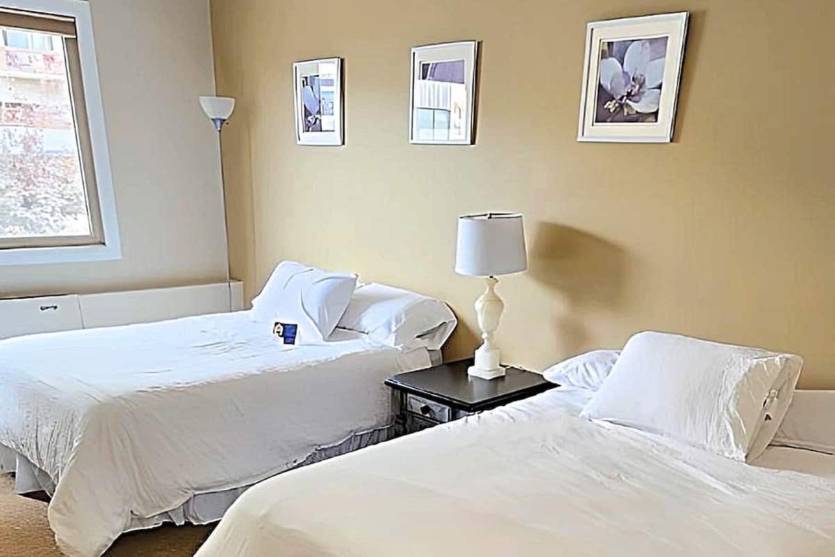 Een hotelkamer met twee bedden, beige wanden en wanddecoraties in lijsten.