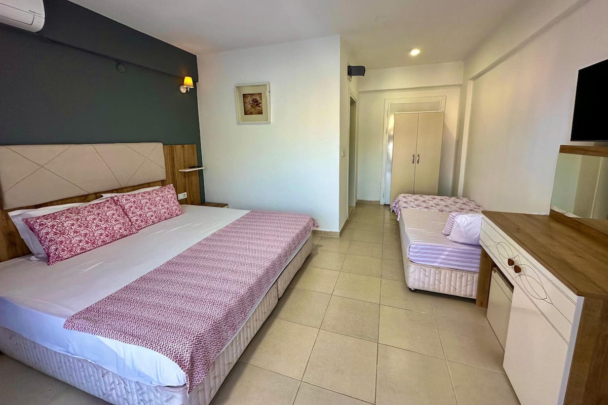 Una camera d'albergo con un letto grande, un letto più piccolo, una scrivania e un armadio.