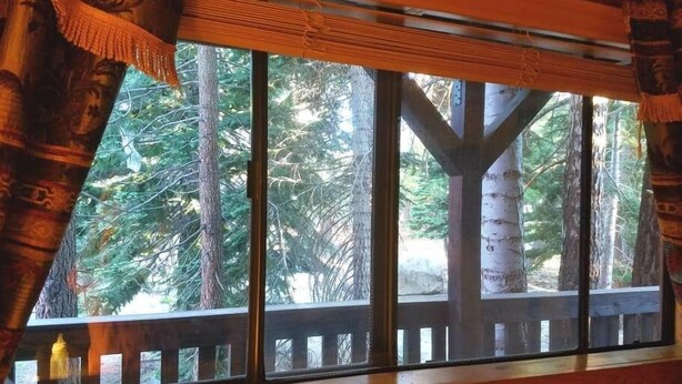 Habitación con un ventanal grande que da a una terraza de madera y un bosque denso.
