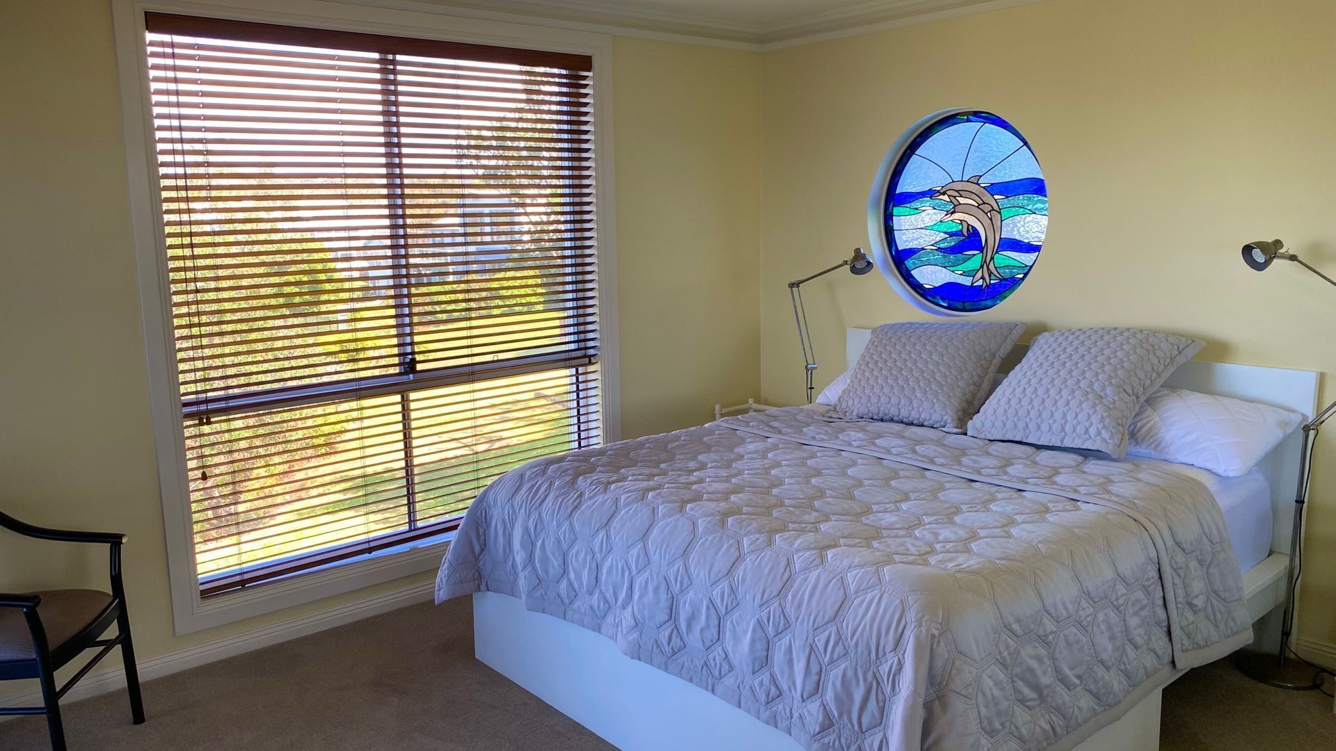 Un dormitorio con un gran ventanal, una cama con cubrecama acolchado y una lámpara de pared.