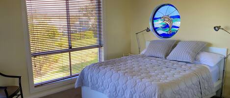 Un dormitorio con un gran ventanal, una cama con cubrecama acolchado y una lámpara de pared.