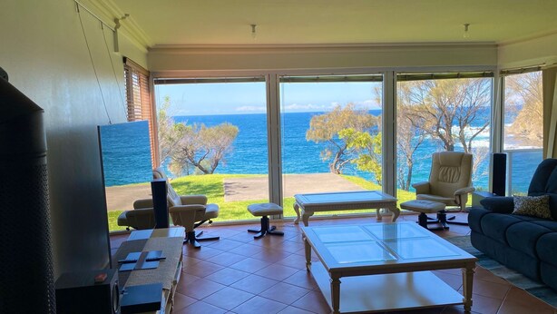 Un salón con un gran ventanal que da a un balcón con vistas al mar.