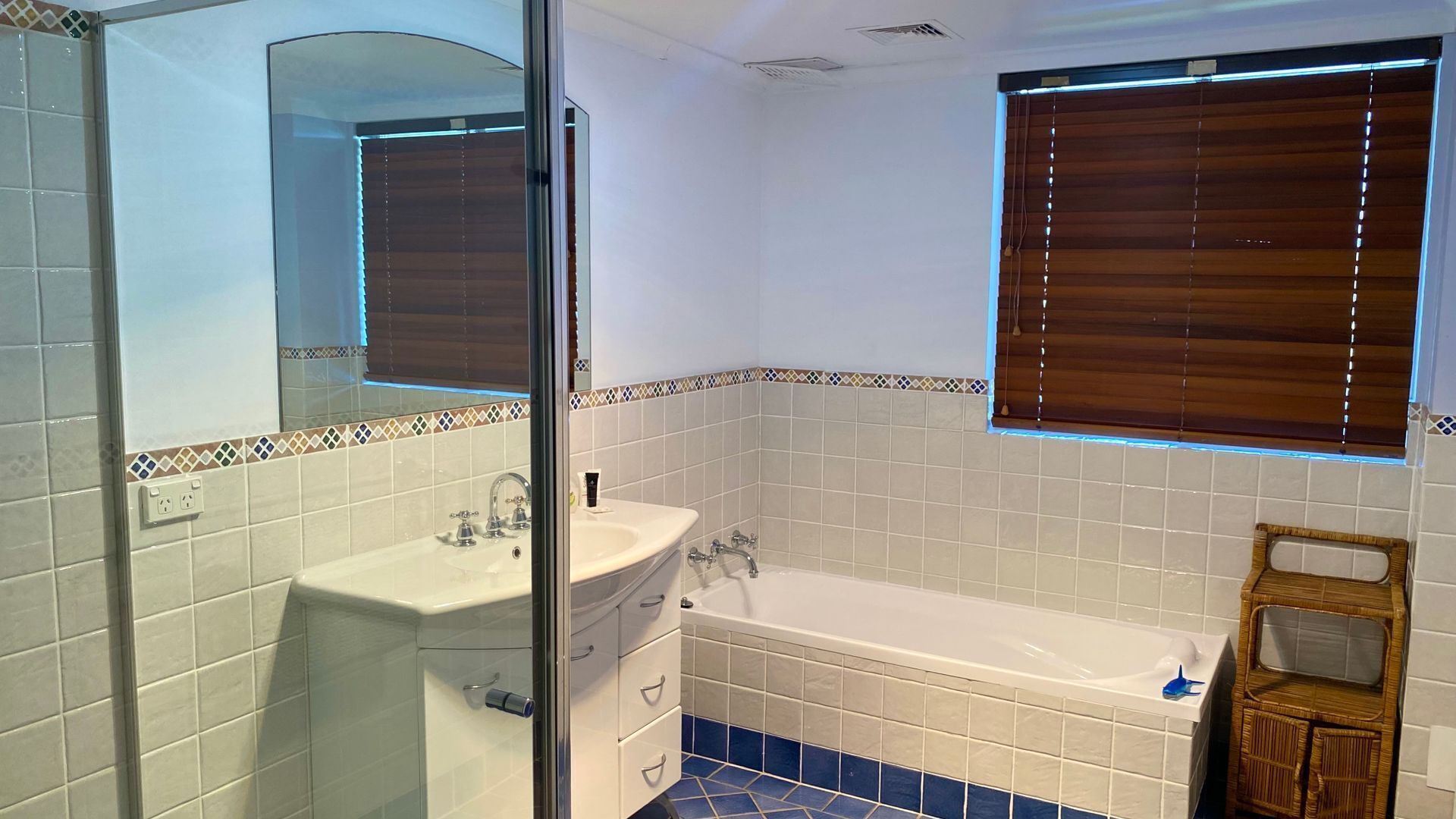 Ein Badezimmer mit einem weißen Waschbecken, einer Badewanne und einem Fenster mit Jalousien.