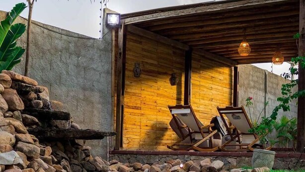 A rustic cabin with a stone wall, a wooden deck, and a small pond. - Pousada Cangaço (Santana Do Ipanema)