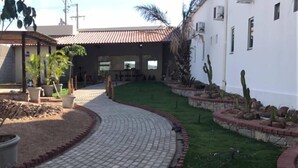 A paved pathway leading to a building with a tiled roof, surrounded by landscaped areas with grass and cacti. - Pousada Cangaço (Santana Do Ipanema)