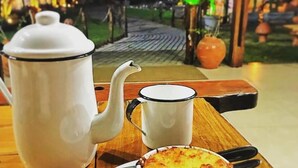 A table with a white teapot, a white cup, and a white bowl with a baked dish. - Pousada Cangaço (Santana Do Ipanema)