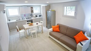 Un espacio habitable compacto con kitchenette, comedor y sofá con cojines naranja.