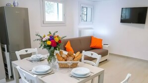 Un comedor con una mesa preparada para cuatro, sillas blancas, un cesto de pan y un jarrón de flores.