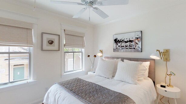 A bedroom with a bed, a ceiling fan, a window with blinds, a bedside table with a lamp, and a wall-mounted artwork. - Heated Pool Access | 5*Clean | Flex Cancelation (Savannah)